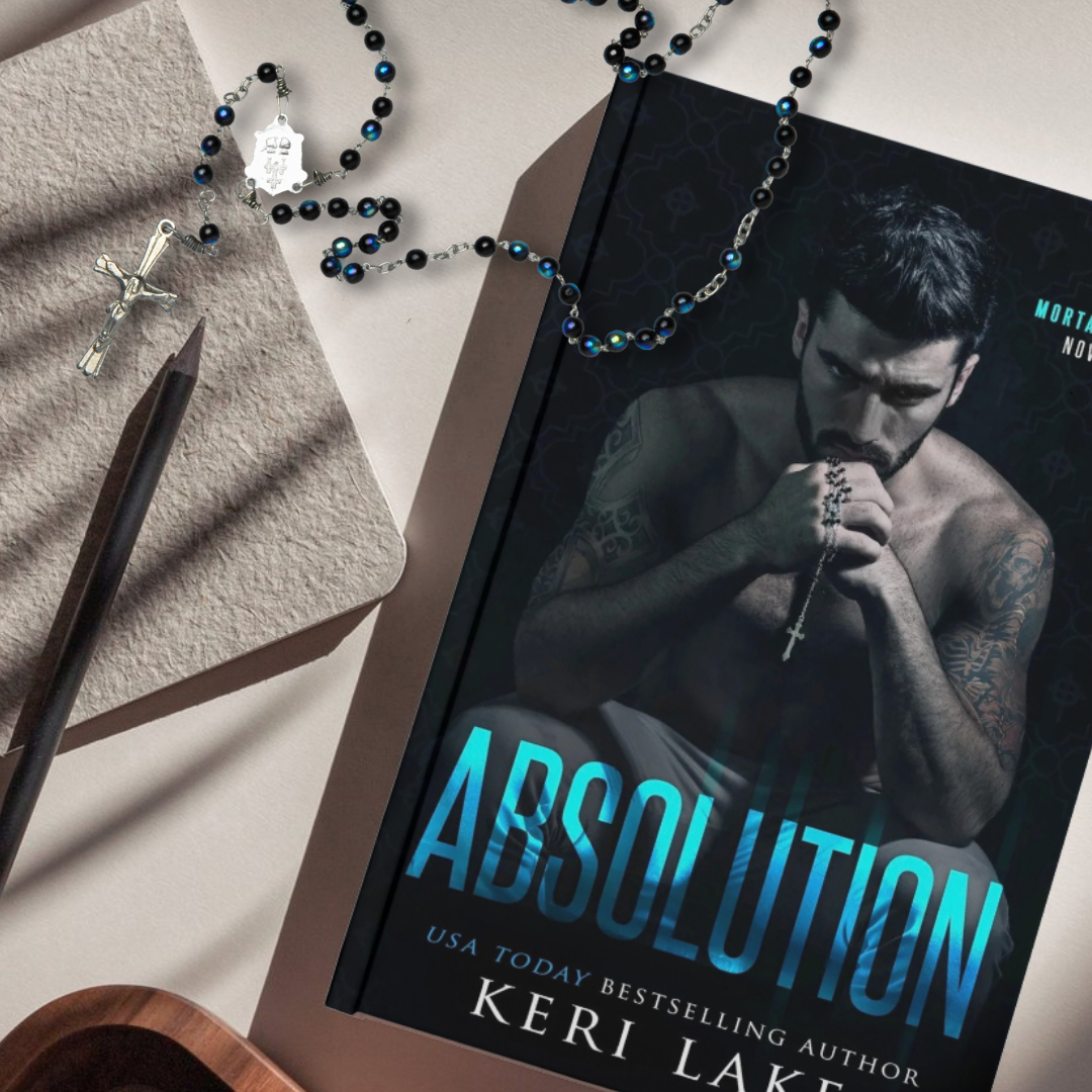 Book titled 'Absolution' by Keri Lake with a rosary and pen on a textured surface